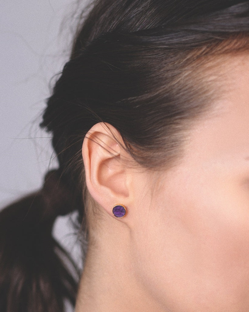 Model wearing Cosmic earrings - Handcrafted birch wood and sterling silver studs with a  orion purple birch wood interior, plated with 24k gold.