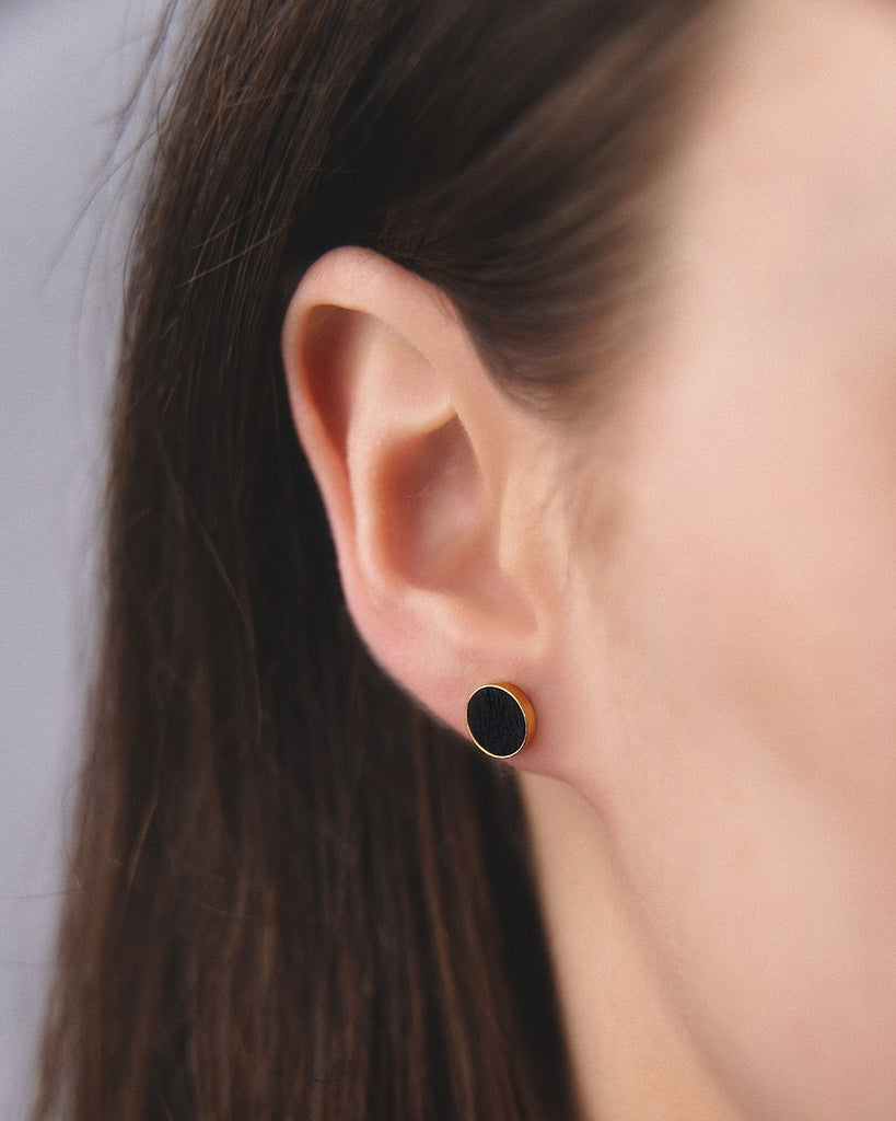 Model wearing Cosmic earrings - Handcrafted birch wood and sterling silver studs with a  gravity black birch wood interior, plated with 24k gold.