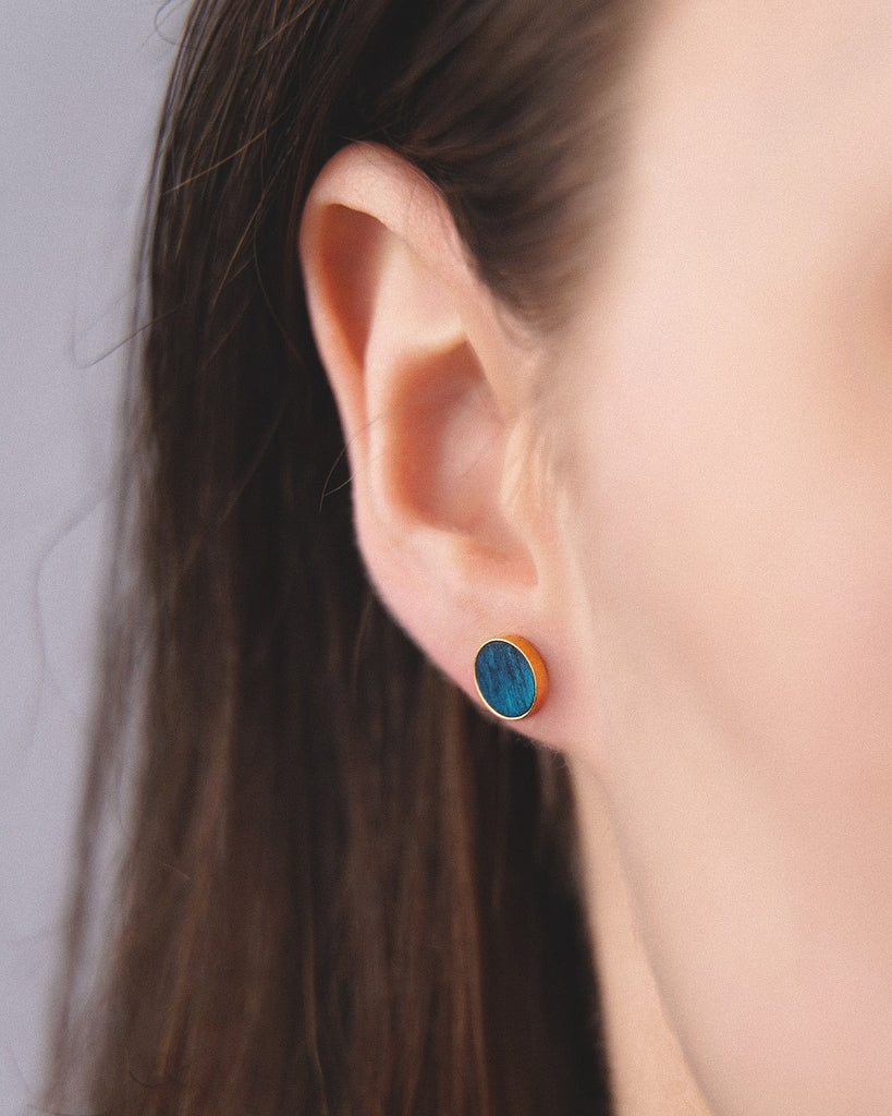 Model wearing Cosmic earrings - Handcrafted birch wood and sterling silver studs with a  supernova blue birch wood interior, plated with 24k gold.