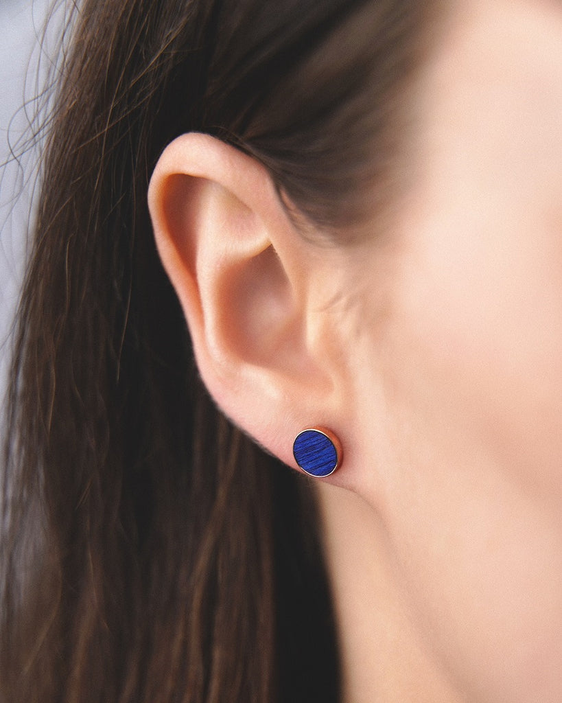 Model wearing Cosmic earrings - Handcrafted birch wood and sterling silver studs with a ocean blue birch wood interior, plated with 18k rose gold.