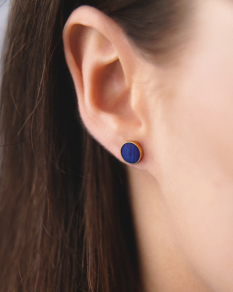 Model wearing Cosmic earrings - Handcrafted birch wood and sterling silver studs with a ocean blue birch wood interior, plated with 24k gold.