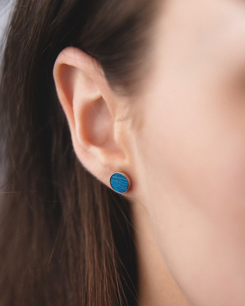 Model wearing Cosmic earrings - Handcrafted birch wood and sterling silver studs with a  supernova blue birch wood interior, plated with platinum.