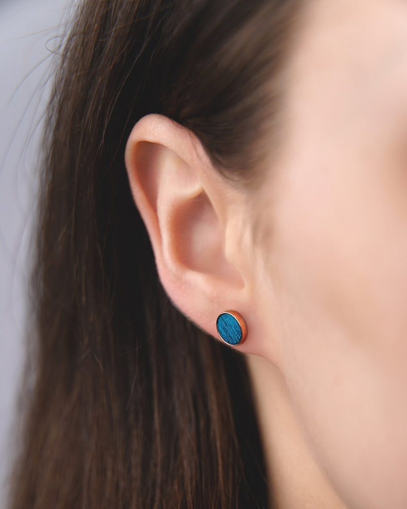 Model wearing Cosmic earrings - Handcrafted birch wood and sterling silver studs with a  supernova blue birch wood interior, plated with 18k rose gold.