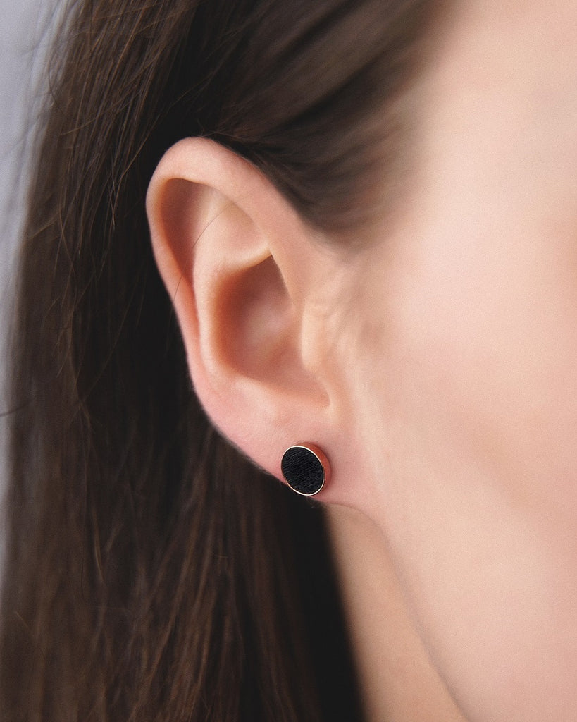Model wearing Cosmic earrings - Handcrafted birch wood and sterling silver studs with a  gravity black birch wood interior, plated with 18k rose gold.